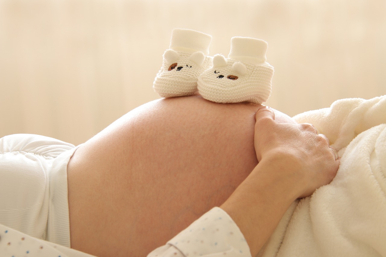 woman with pregnant belly and small infant slippers on top. fertility, preconception, infertility, wellness