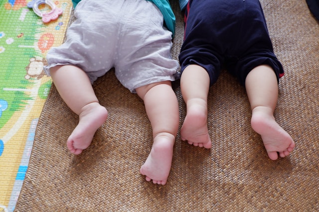 Two babies laying on their stomachs showing baby feet. 