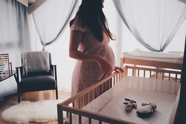 Pregnant woman looking at a crib with baby toys in it.