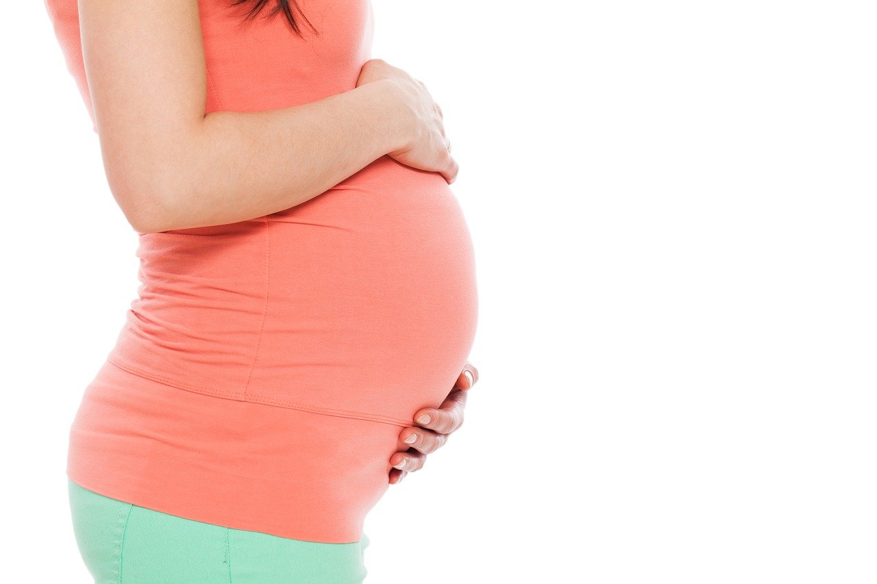 Pregnant woman in a peach top holding her baby bump.