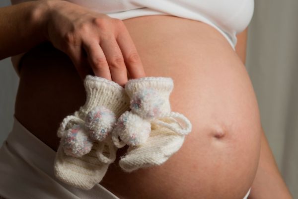 Woman holding baby booties near her pregnant belly