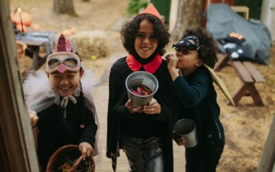 Children in Halloween costumes, smiling and holding buckets, celebrating the holiday spirit and enjoying treats.